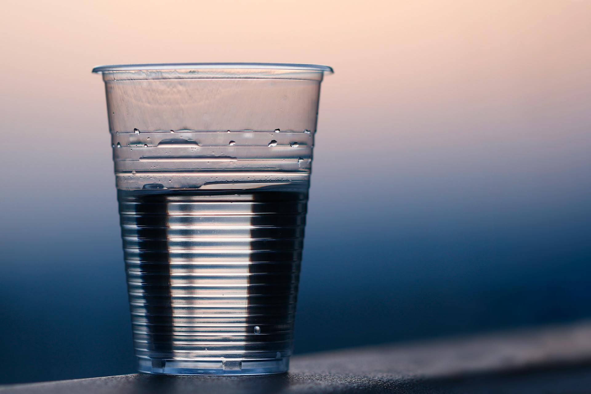 Clear plastic cup filled with water against a soft gradient background
