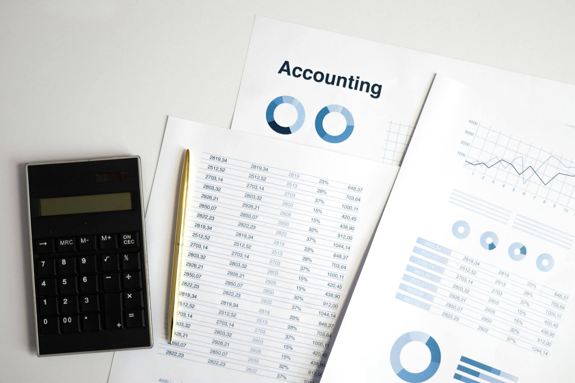 A tidy accounting workspace featuring a calculator, gold pen, and printed financial reports with charts, graphs, and numerical data, capturing the look and feel of organised financial analysis.